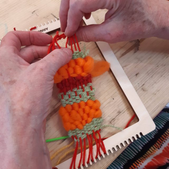 A coloured photograph of a person weaving bright orange, mint green, and red.