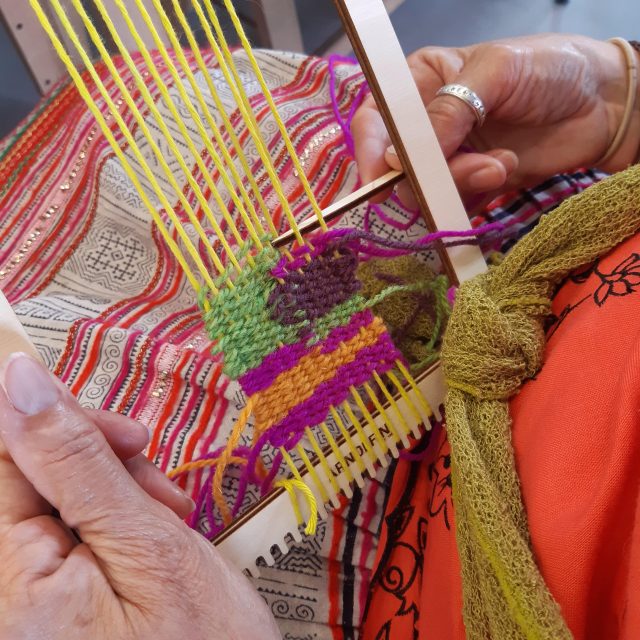A coloured photograph of a person weaving bright yellow, green, red and orange.