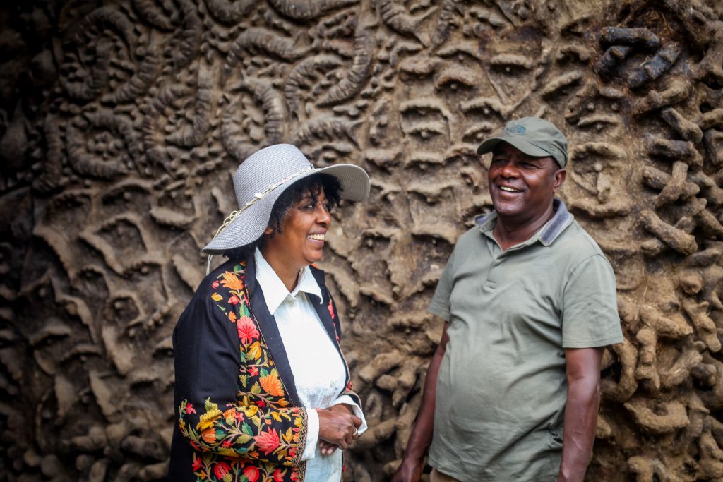 a colour photograph of Meskerem Assegued and Elias Sime against the backdrop of the clay clad wall of Zoma Museum.